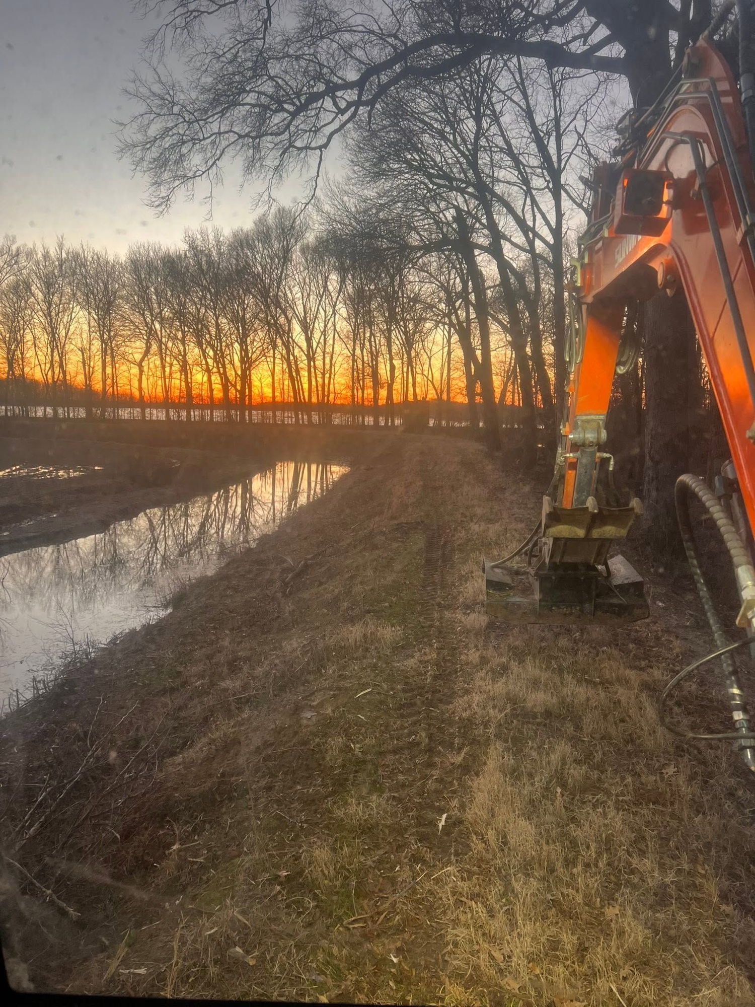 Sunward mini excavator building a berm along a duck hunting impoundment at sunset