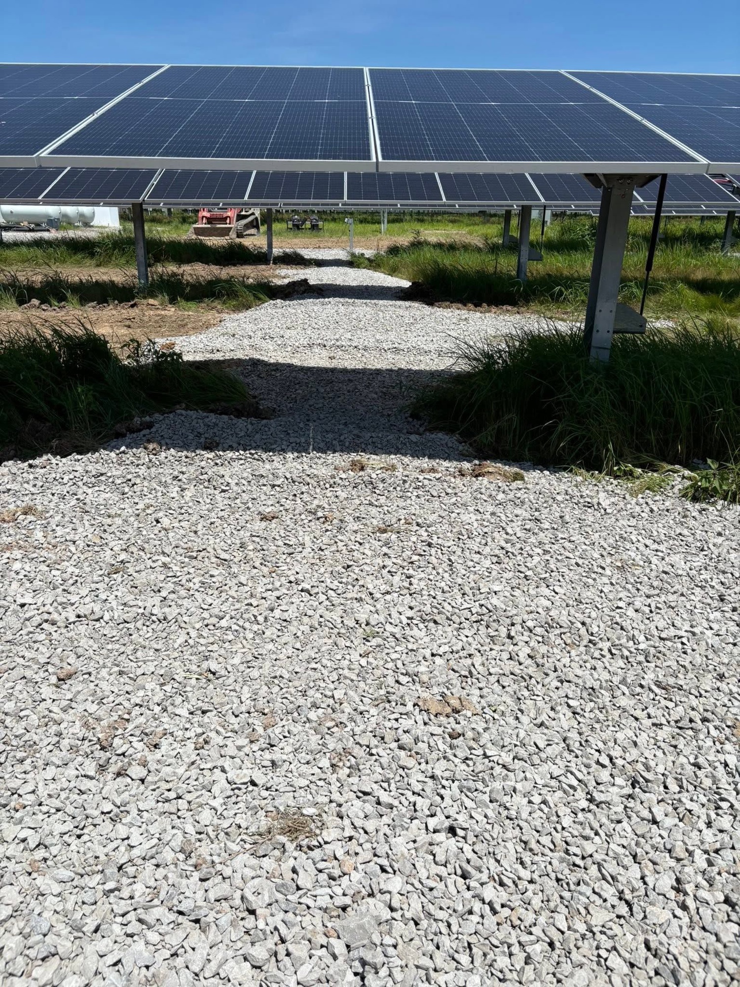 Gravel access road under construction between rows of solar panels