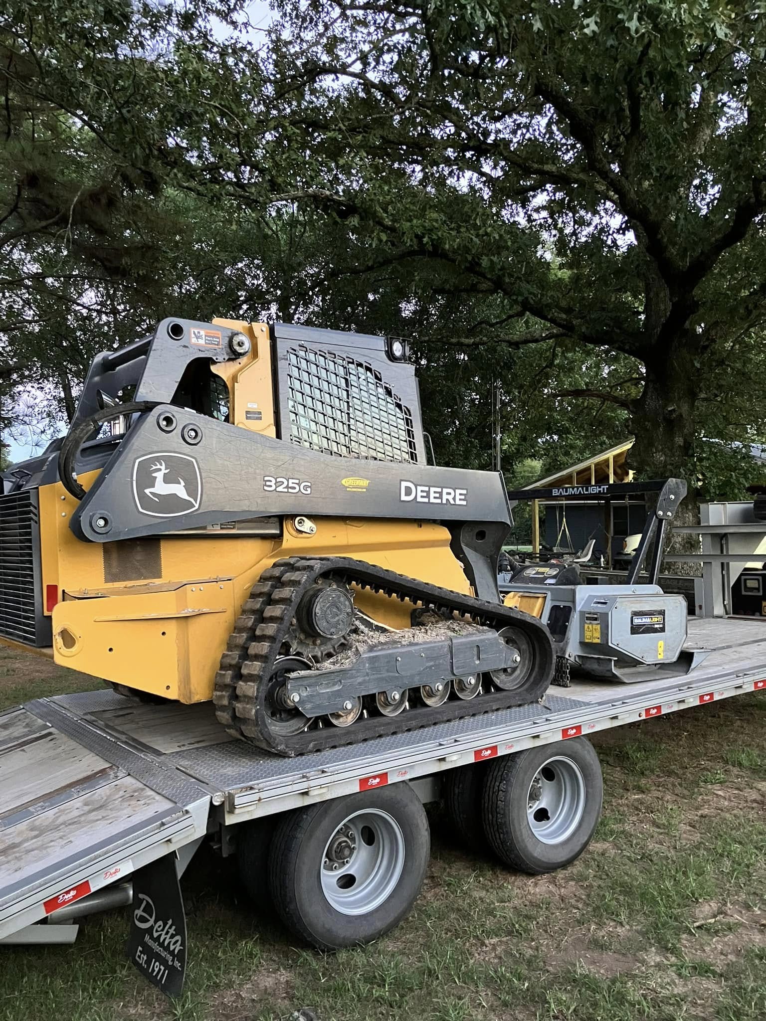 John Deere 325G with Baumalight mulching head loaded on a trailer, ready to head to the job site
